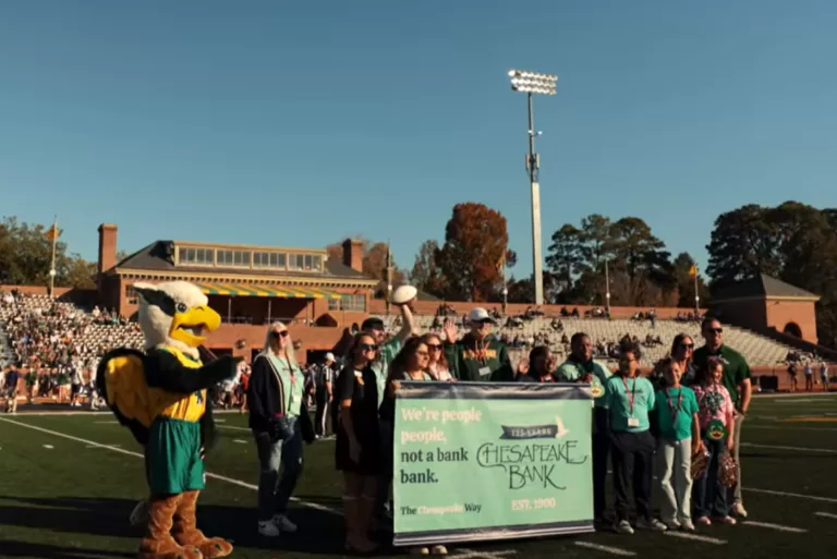 William and Mary x Ches Bank sponsorship football game on the field holding "We're People People" banner.